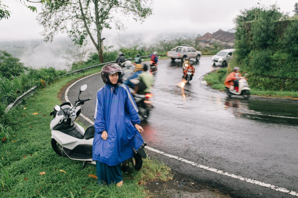 a woman in raincoat sitting on a motorcycle beside the road
